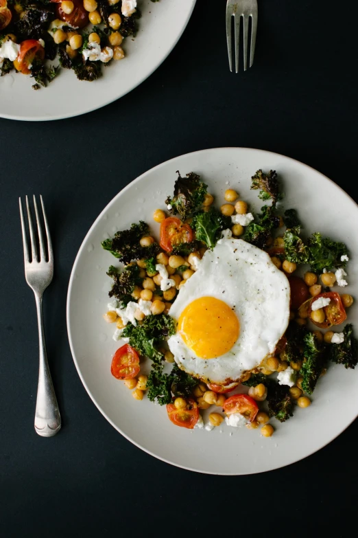 two plates with eggs, vegetables, and sauce on them