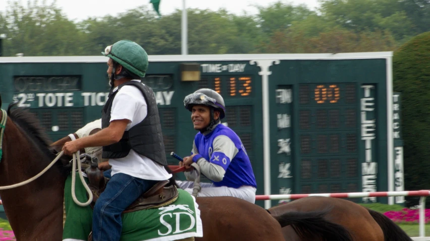 two jockeys are on horseback at the track