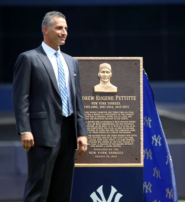 a smiling man stands by a sign with a statue of a baseball player