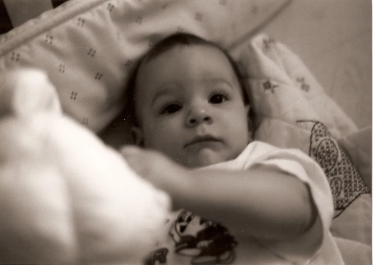 a baby in bed with its hand extended out toward him