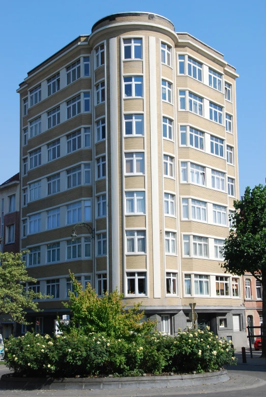 a tall tan building with lots of windows near a tree