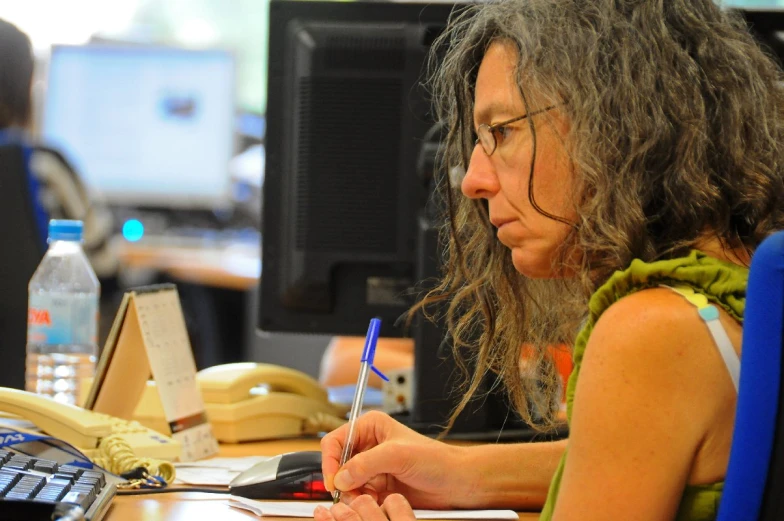 a woman sitting at a computer desk with a pen and paper