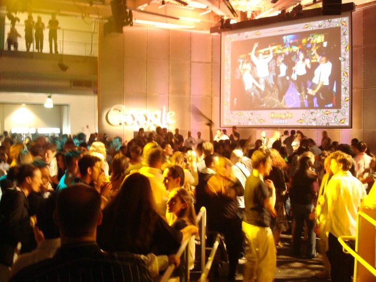 a crowd of people stand in front of a large television screen
