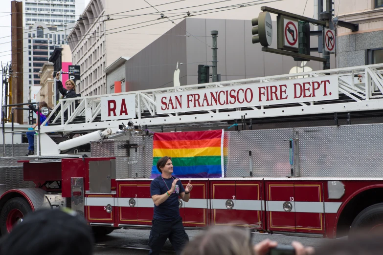 people watch a firetruck carrying a rainbow flag