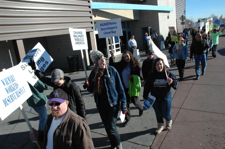 group of people walk down a sidewalk with protest signs