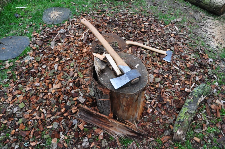 some axes sitting on a stump in the dirt