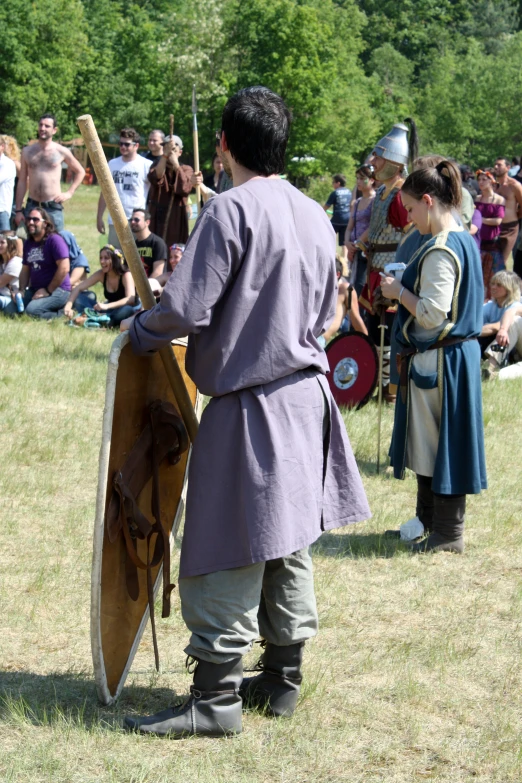 a man in a historical costume holds a shield and sword as others stand behind him