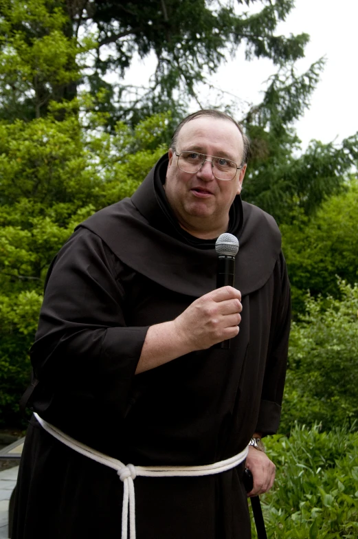 an older man in a black robe is standing and holding a microphone