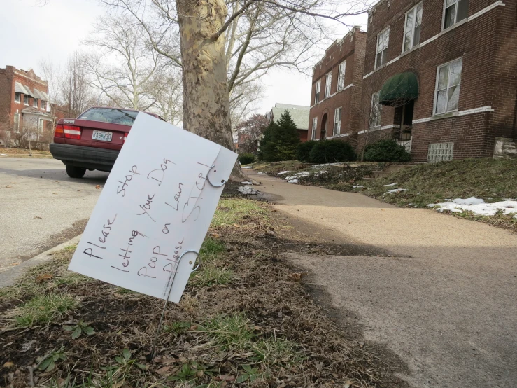 a sign posted on the grass in front of a tree