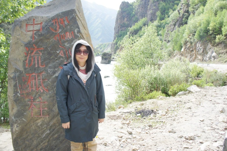 the woman poses near a huge stone with writing on it