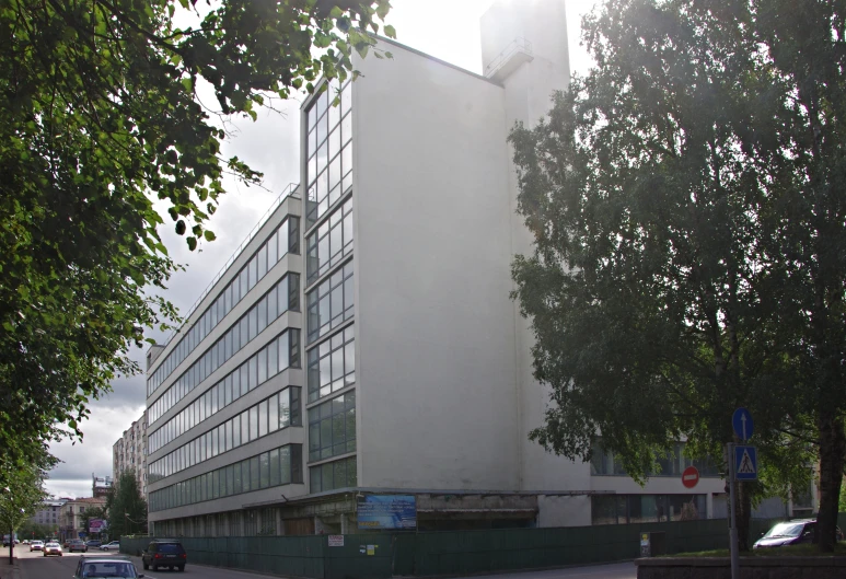 a big white building near some trees with cars parked on the side