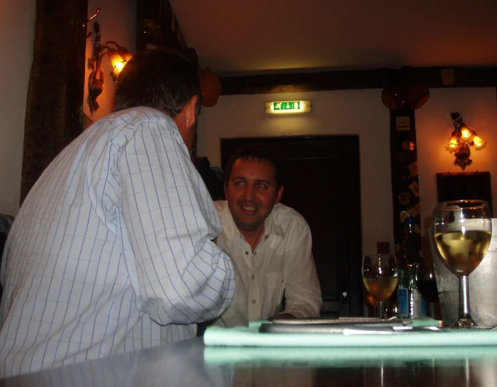 two men sitting at a bar laughing with drinks