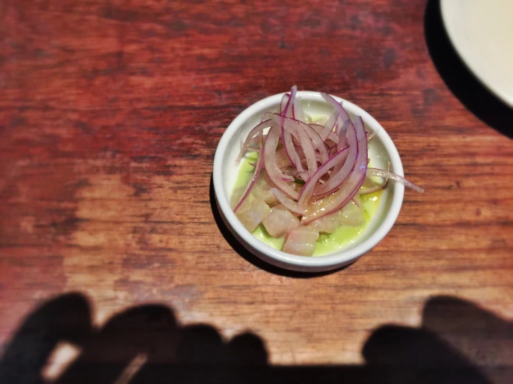 a white bowl with some onion in it on a wooden table