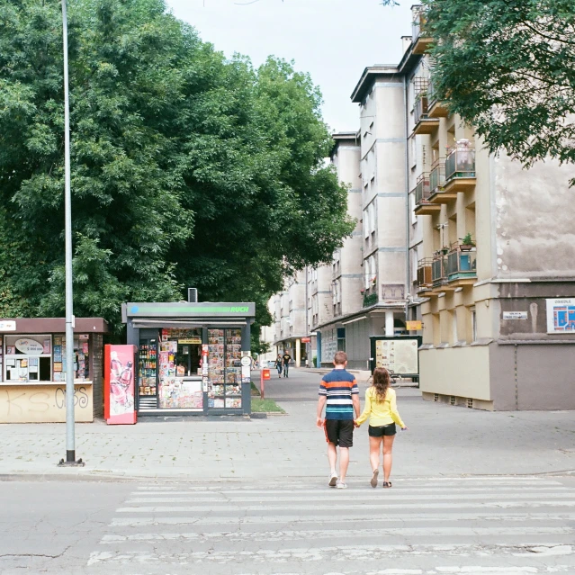 two people are walking down the street towards a kiosk