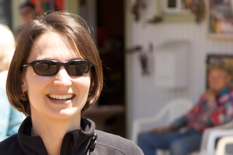 a smiling woman wearing sunglasses and a black coat