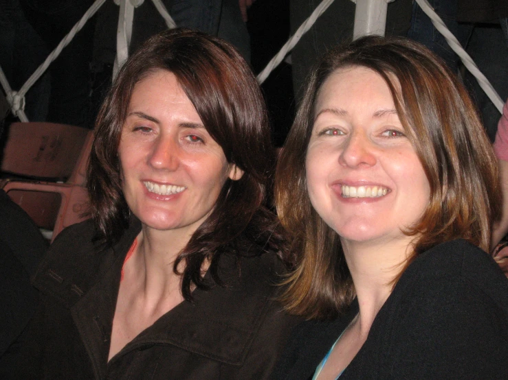 two women are sitting and smiling while looking at the camera