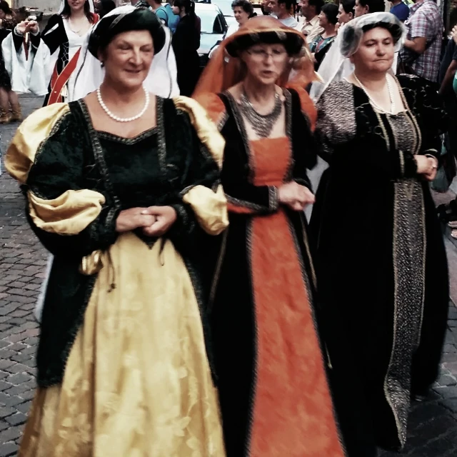 three women in old dress are walking down the street