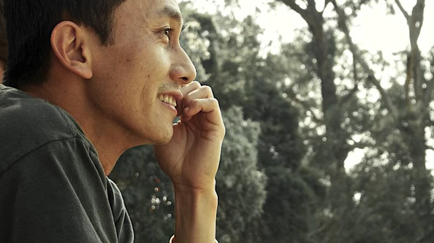 a man talking on a cell phone next to trees