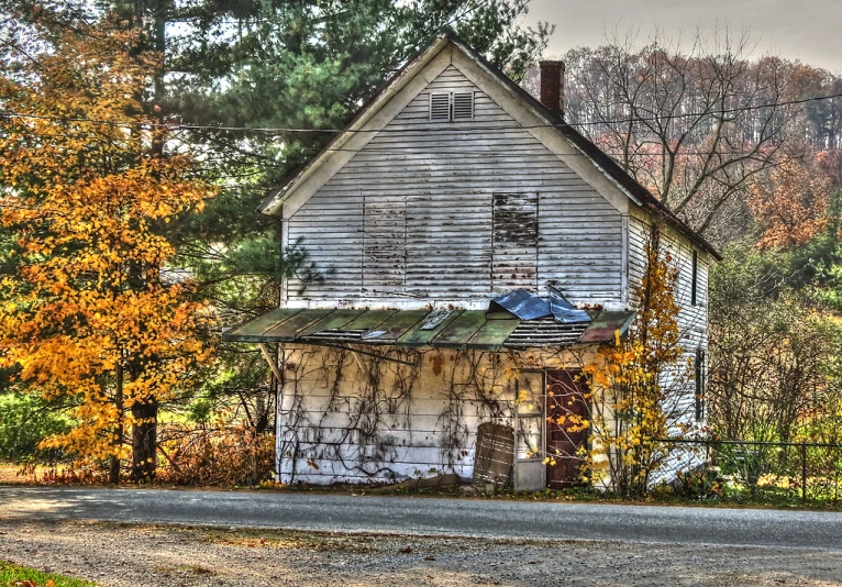 a run down white house sits abandoned in autumn