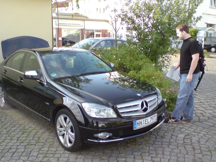 the young man is standing next to his black car