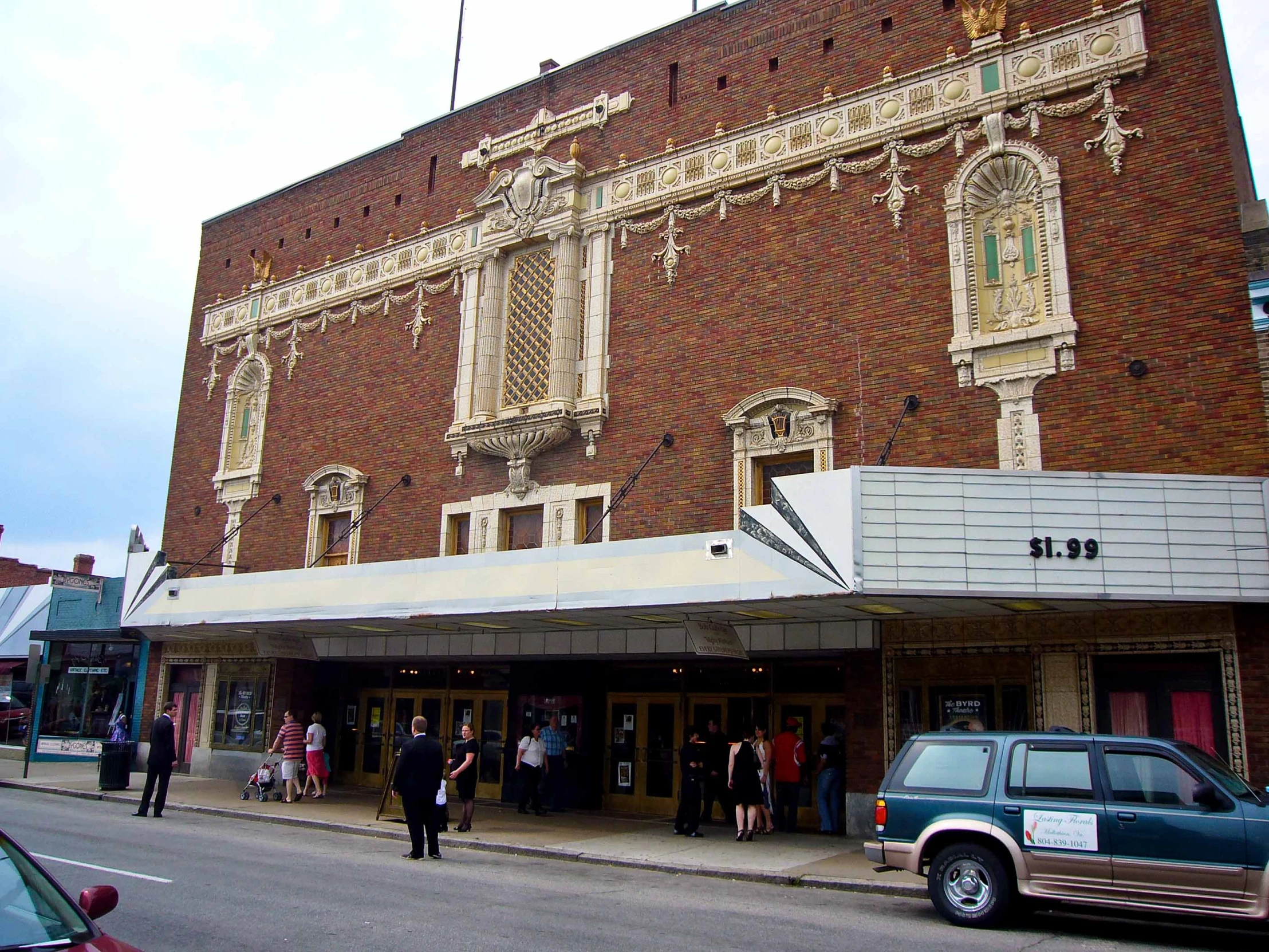 a brick theater on the corner with a car parked nearby