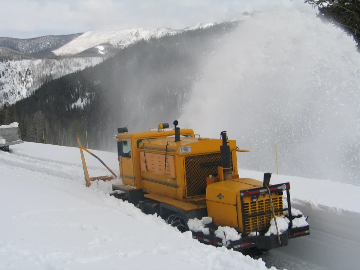 a yellow machine dumping snow onto some slopes