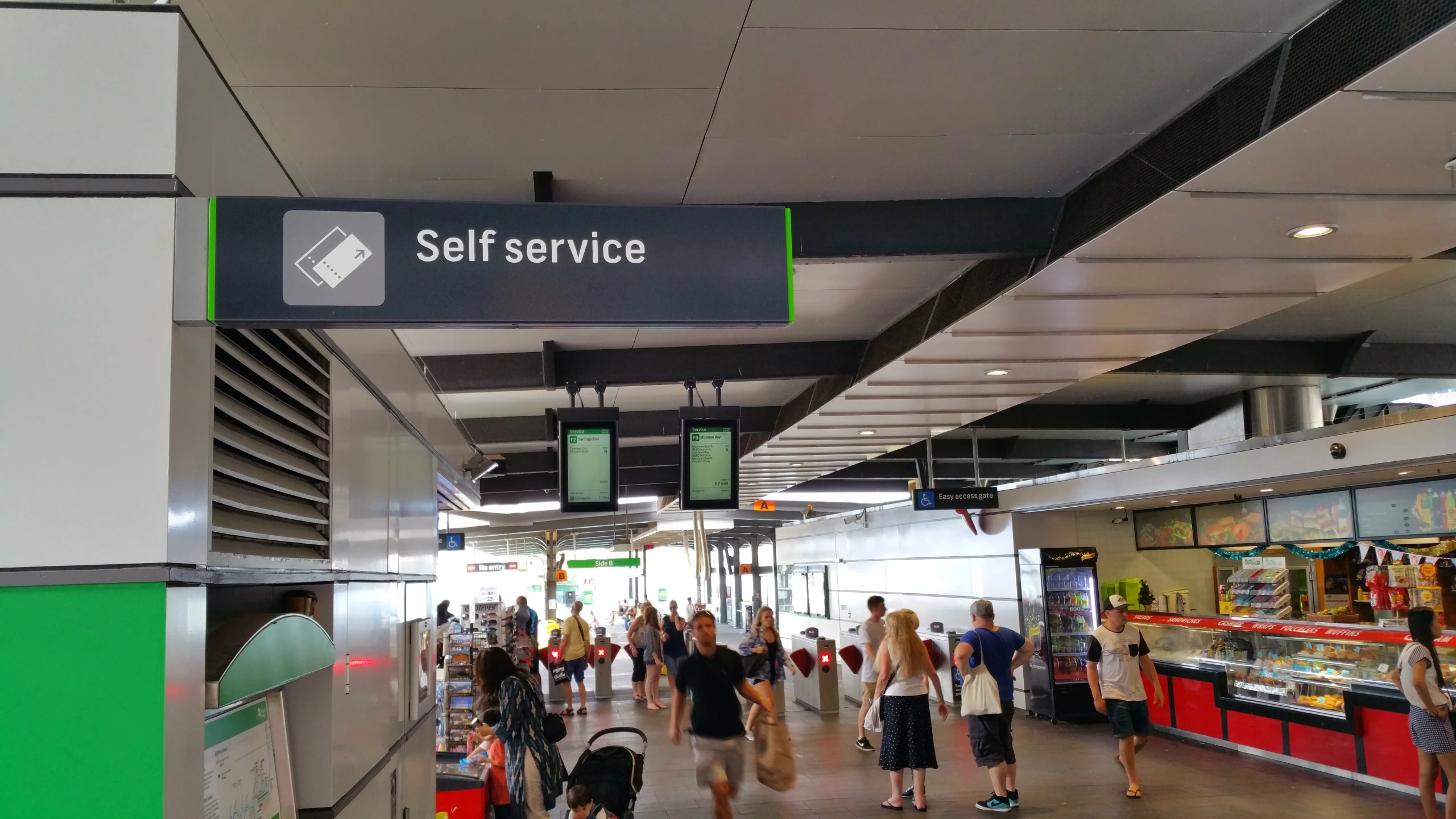 many people walk through an airport terminal with a self service sign