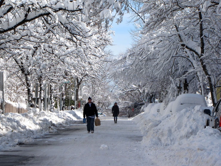 two people walk down a snowy street on a sunny day