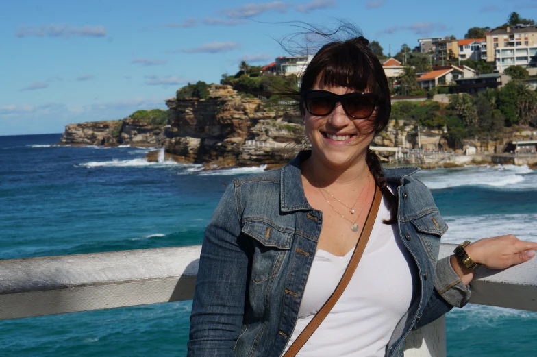 a woman smiling for the camera while standing on a pier with an ocean view