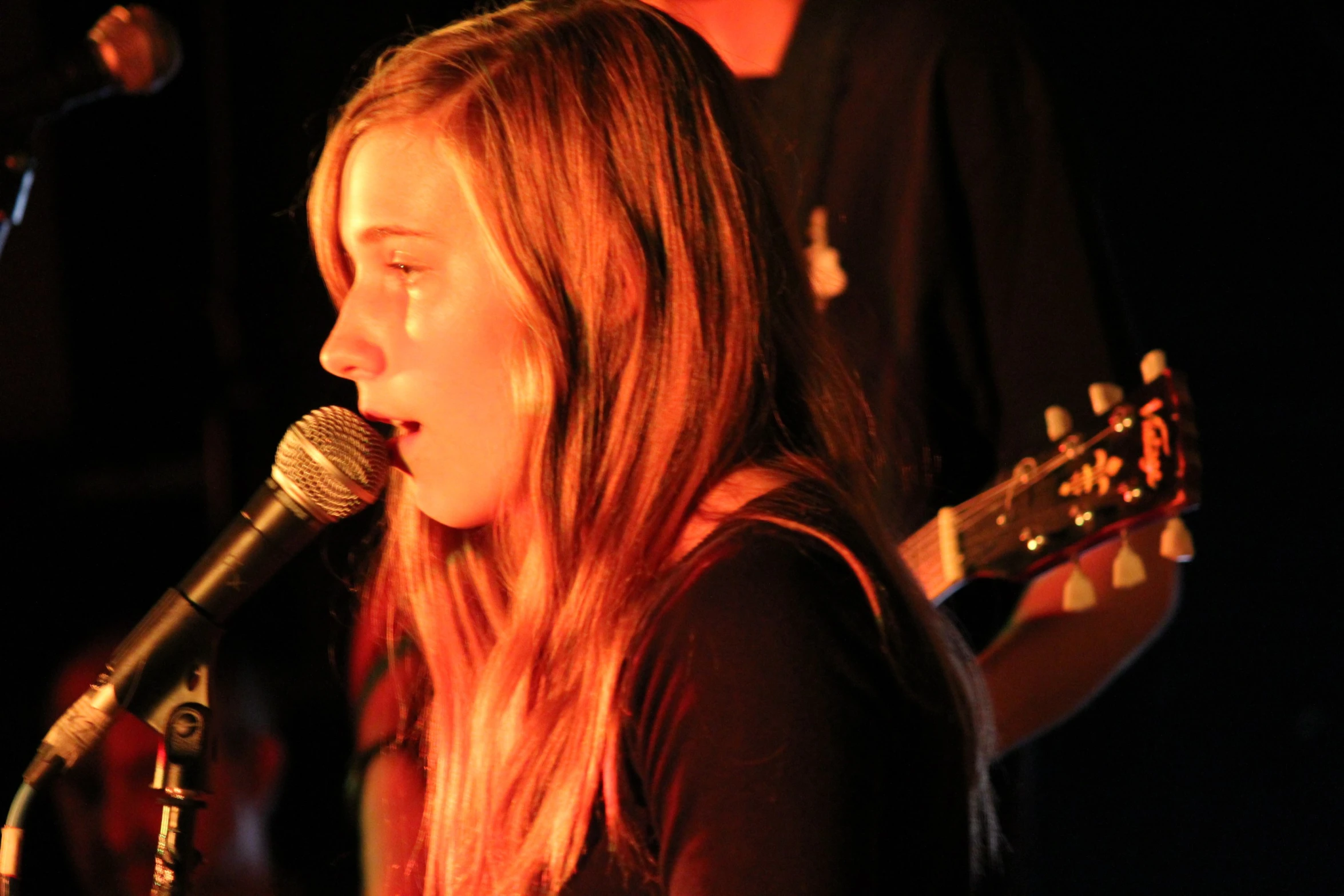 a girl in concert playing guitar with a microphone