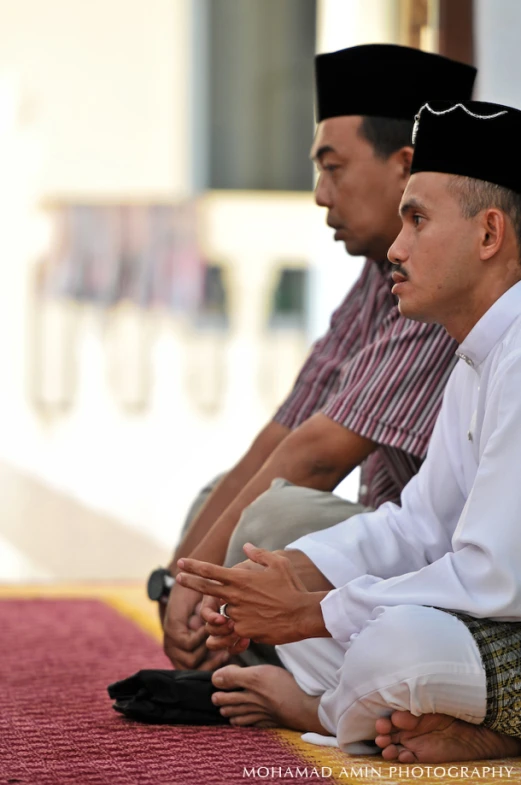 three men sitting together on benches wearing hats