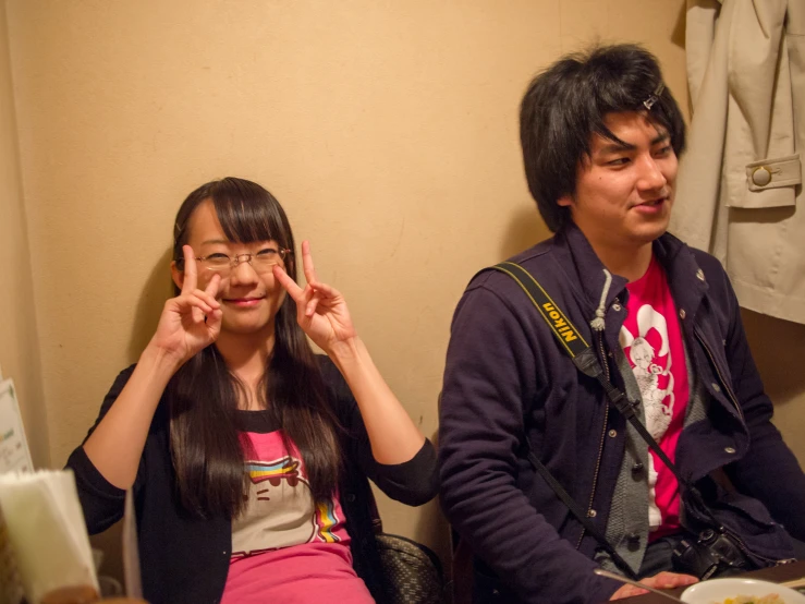 a girl and boy sitting at a table with their hands up