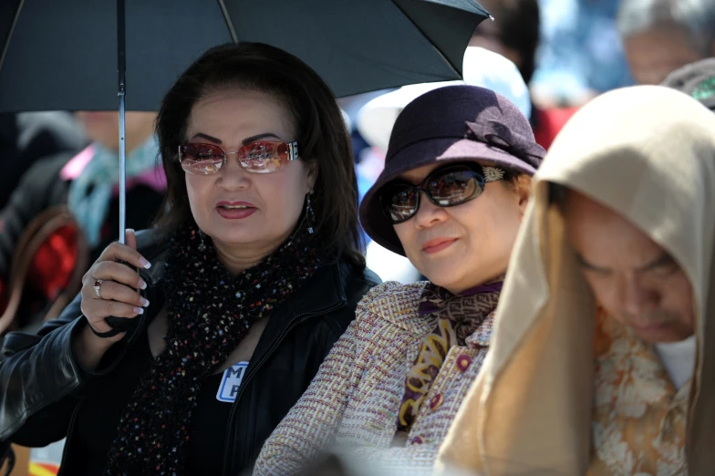 two ladies sitting next to each other one holding an umbrella