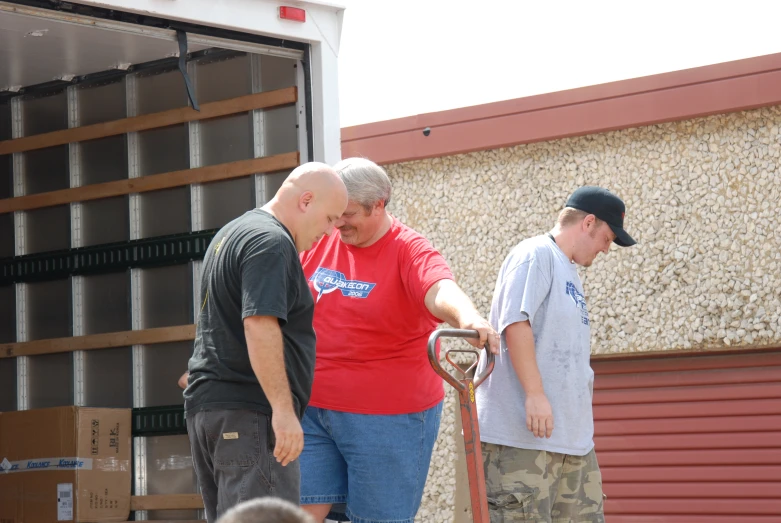 three people loading soing onto a truck in front of a storage compartment