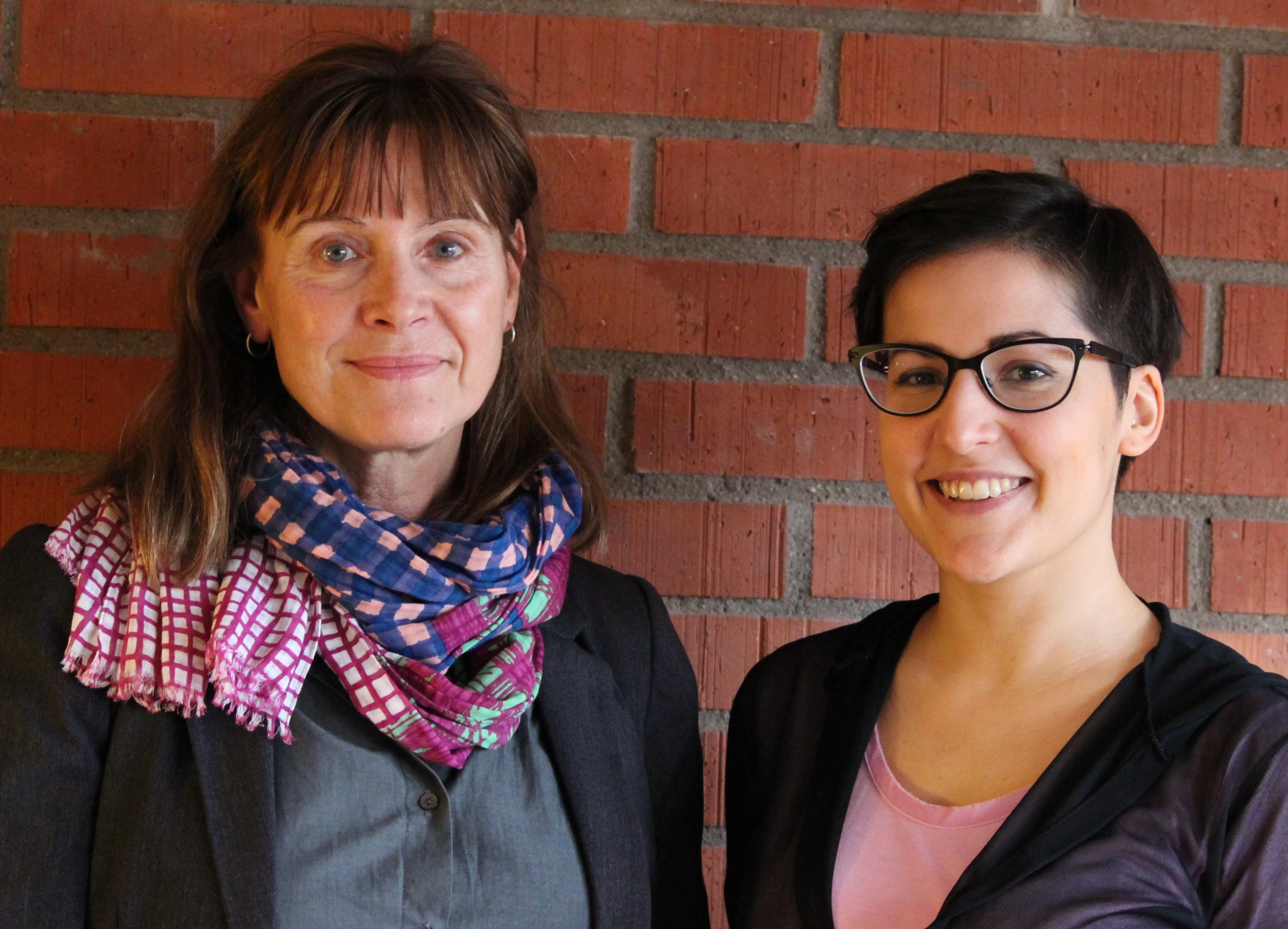 two women are standing against a brick wall