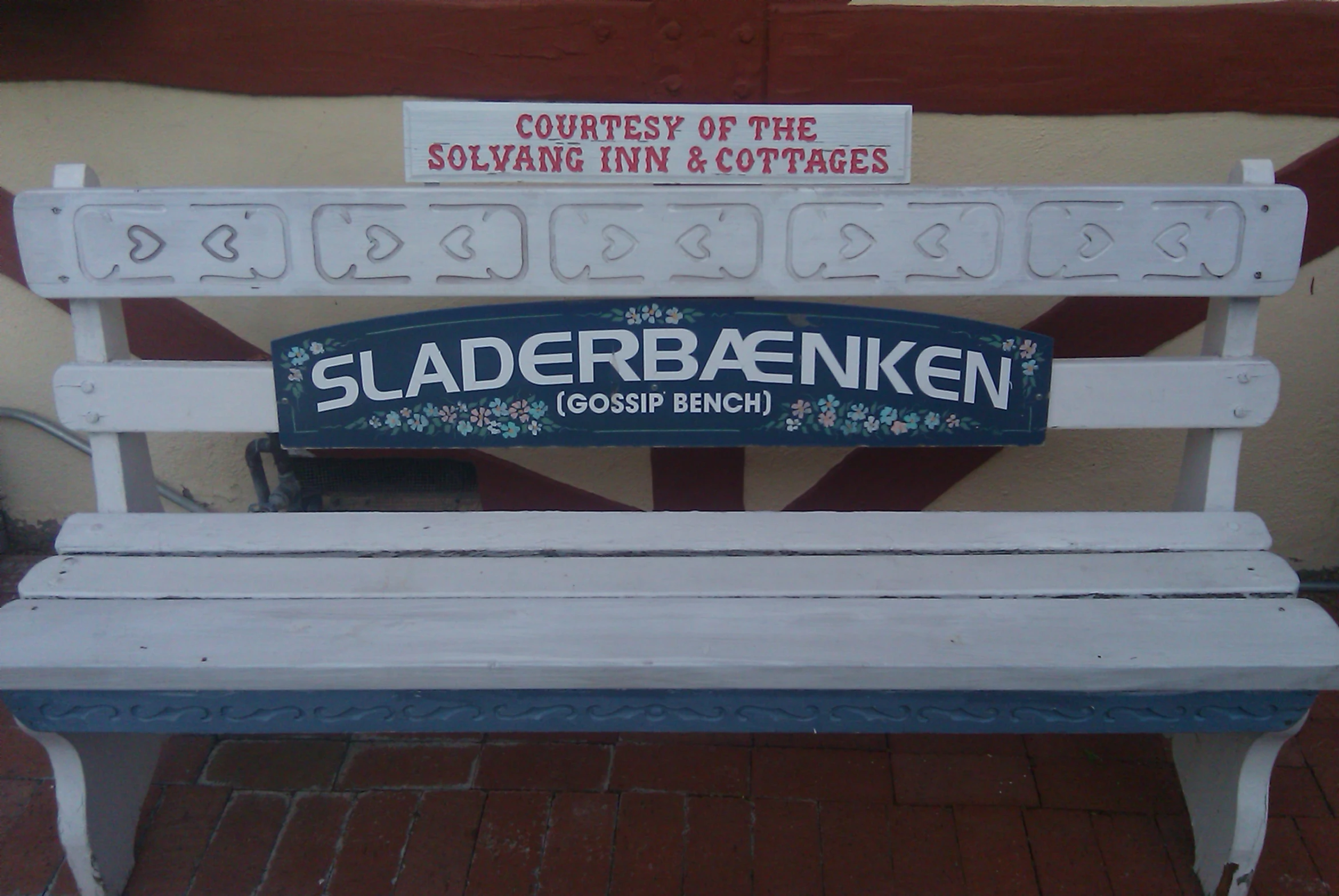 a wooden bench is on the sidewalk beside a sign