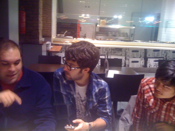 a group of three men sit around looking at their phones