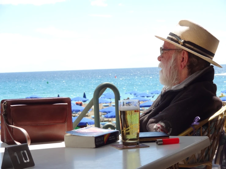 a man with a hat and glasses sitting at a table near the beach