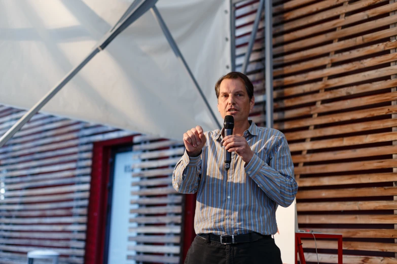 a man holding a microphone standing in front of a wooden wall