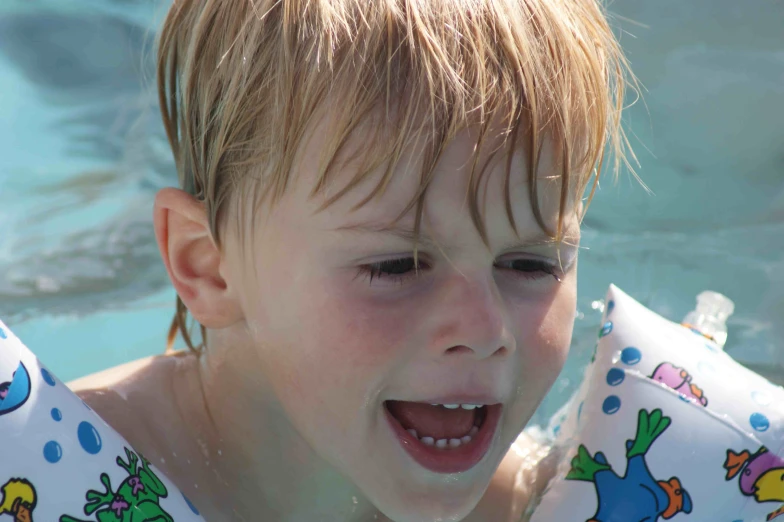 young blonde child swimming in pool holding water bottle