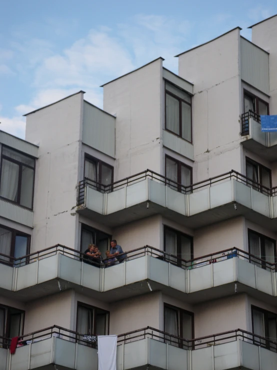 people sit at the balconies outside an apartment building