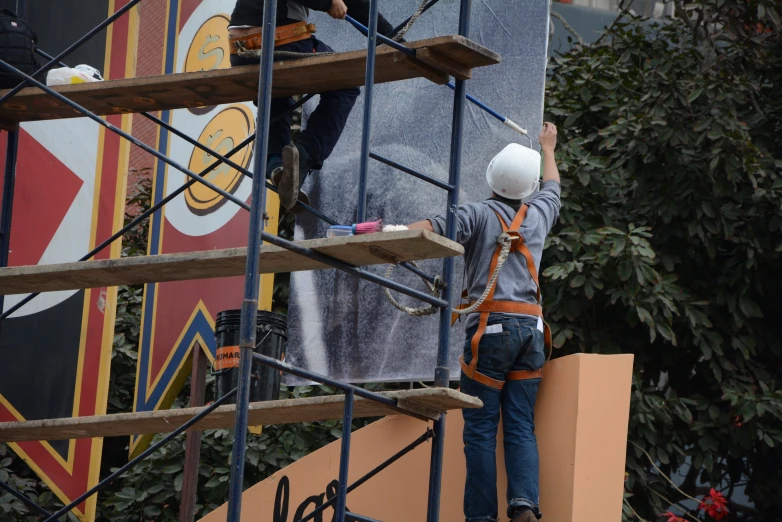 two men on scaffolding working to decorate a mural