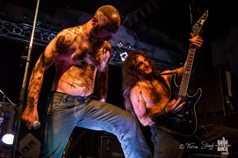 two men with painted body paint playing guitar in a rock concert