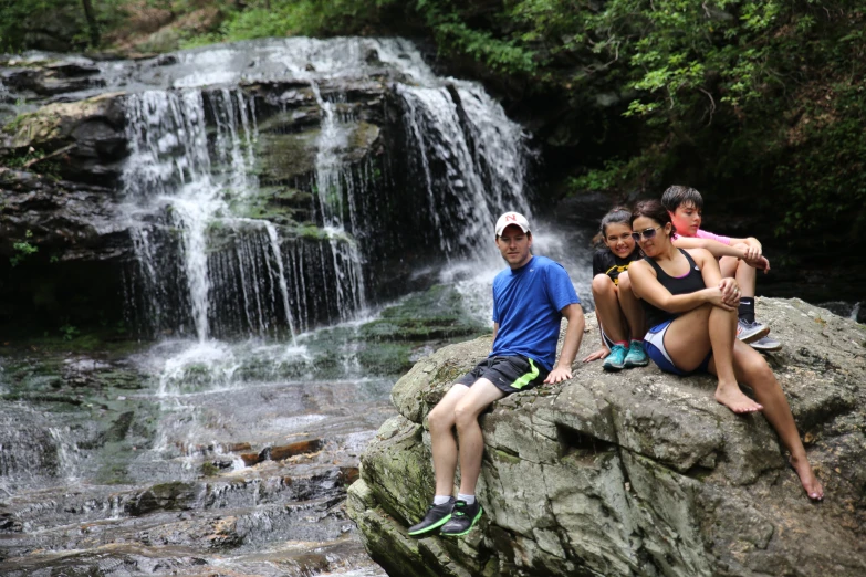 four children are sitting at the base of a waterfall