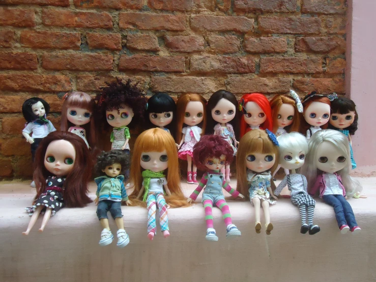 a bunch of dolls and other toys by a brick wall