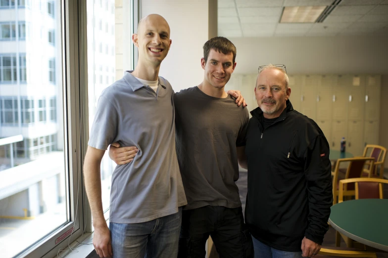 three men standing next to each other in front of a window