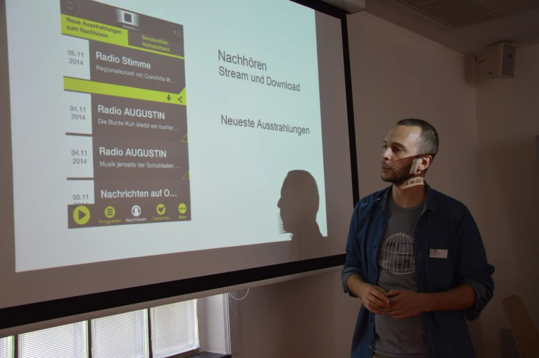 man standing by big projection screen, holding cellphone to his ear