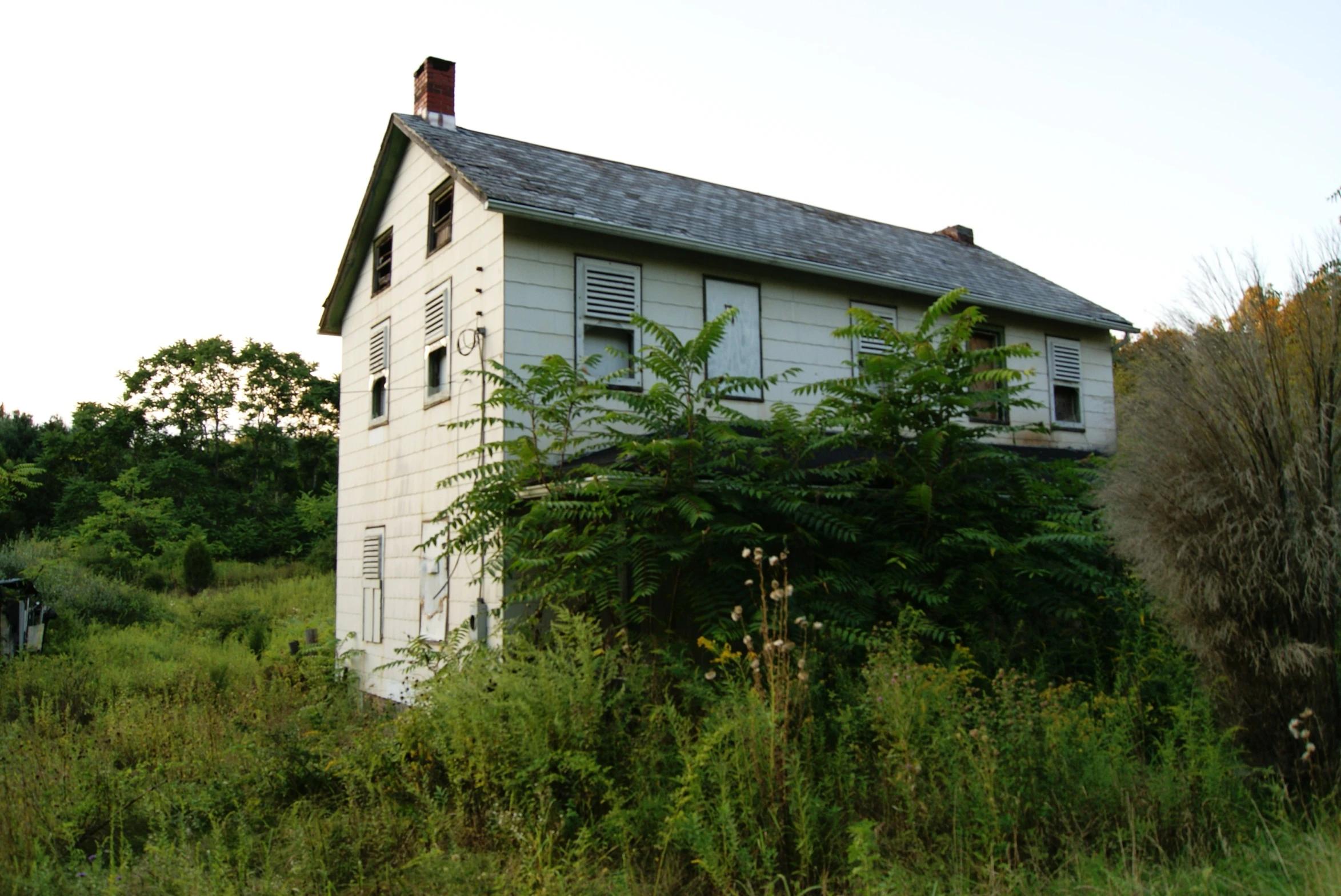 an old white run down house in a grassy field