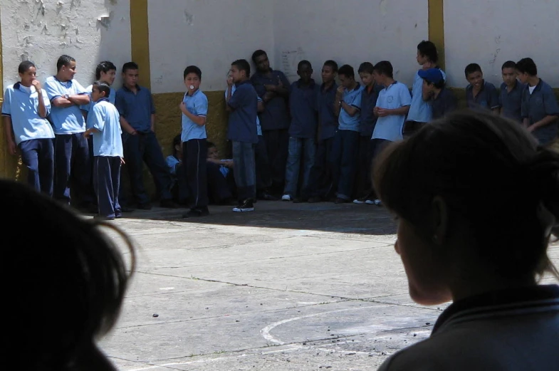 a crowd stands near the back wall of an open building while several children stand in the background