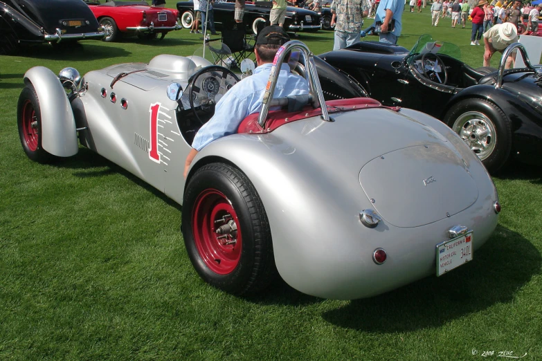 two people are driving a vintage car in a grassy area